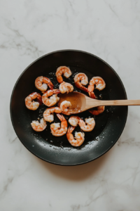 This image shows shrimp sizzling on one side in a hot skillet, turning golden and slightly crisp, ready to be flipped for even cooking.