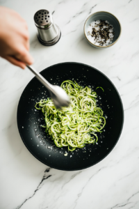 This image shows spiralized zucchini noodles being sautéed in butter, seasoned lightly with salt and pepper.