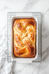 This image shows the freshly baked loaf of cinnamon swirl bread resting on a wire rack, cooling to room temperature before being sliced and served.