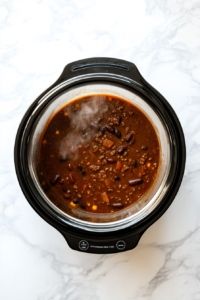 This image shows the slow cooker lid being placed on top, beginning the process of slow cooking the chili to perfection over several hours.