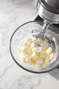 mixing bowl where the prepared dry ingredients are being gradually added to the wet mixture of butter, sugar, eggs, and vanilla to form a smooth cookie dough.