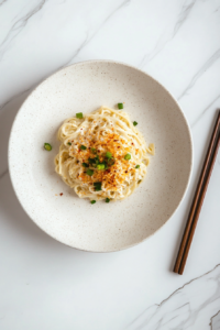 This image shows a plate of creamy garlic noodles ready to be enjoyed, garnished with vibrant spring onions and chili flakes, making it a visually stunning and delicious meal.