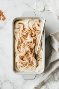 This image shows a knife being used to swirl through the batter in the loaf pan, creating a decorative cinnamon swirl pattern that will bake into the bread.