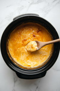 This image shows the ingredients for Buffalo Chicken Dip being cooked together in the crockpot to combine the chicken, cheeses, and sauces evenly.