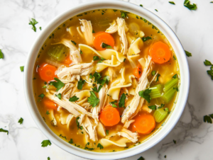 This image shows a comforting bowl of Crockpot Chicken Noodle Soup, featuring tender noodles, shredded chicken, and pieces of carrots and beans in a flavorful broth, served in a white bowl.