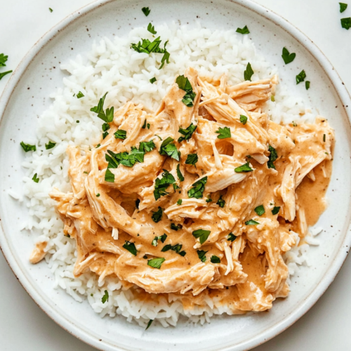 white round plate with creamy Crockpot Italian Chicken topped with Italian seasoning, cream cheese, and cilantro for a flavorful presentation.