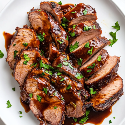 this image shows round white plate holds a tender crockpot pork tenderloin soaked in a rich sauce made from BBQ sauce, mustard, chili powder, and spices, served as a comforting and hearty dish.