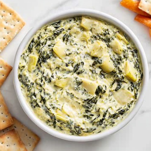 This image shows a white bowl filled with creamy crockpot spinach artichoke dip, topped with sautéed onions, jalapeño peppers, and other vegetables, served as a flavorful appetizer.