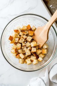 This image shows bread being cubed and seasoned with olive oil and herbs, ready to be baked into croutons for the salad.