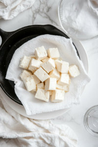 This image shows tofu being pressed with a heavy object to remove excess water, preparing it for the vegan fried chicken recipe.