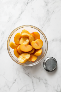 This image shows sliced peaches being thoroughly drained in a strainer to remove excess liquid, ensuring they are ready for use in the cream pie filling.