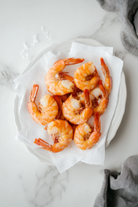 This image shows golden fried shrimp resting on a paper towel-lined plate to remove excess oil, ensuring a light and crispy bite.