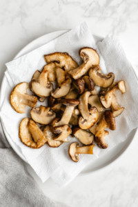 this image shows Freshly fried golden brown oyster mushrooms placed on a paper towel to remove excess oil, ensuring a crispy and light texture.