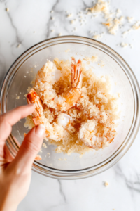 this image shows Shrimp being dipped into a dry breading mixture to begin the coating process for keto coconut shrimp.