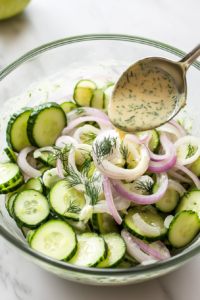 This image shows the creamy dressing being poured over the cucumber and onion mixture, ready to coat the vegetables for a delicious salad.