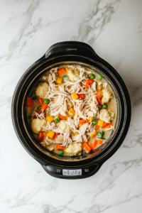 This image shows the completed crockpot chicken and dumplings, with biscuit strips cooked to perfection and the dish steaming hot, ready to serve.