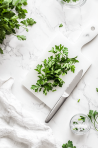 This image shows vibrant green parsley leaves being chopped on a cutting board with a sharp knife, ready to garnish the garlic butter steak bites.