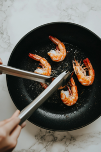 This image shows shrimp being flipped in the skillet to ensure even cooking on both sides, preparing for the final sauce to be added.