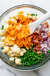 This image shows ingredients like peas, bacon, and cheese being gently folded together in a large mixing bowl to ensure even distribution.