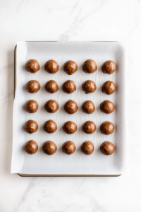 This image shows a tray of cookie dough balls baking in the oven, transforming into golden, low-calorie chocolate chip cookies.