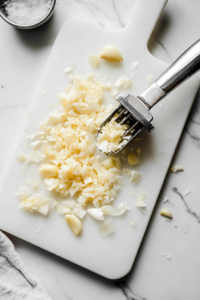 This image shows fresh garlic cloves being peeled and finely minced on a wooden cutting board, essential for making the rich garlic butter sauce for steak bites.