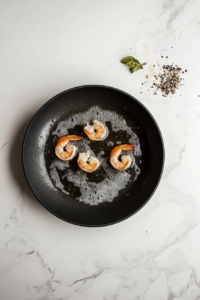 this image shows Shrimp frying in a skillet filled with oil, turning golden brown as they cook.