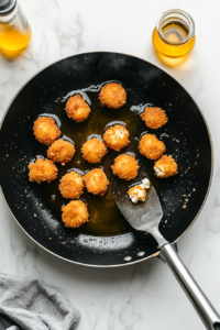 This image shows tofu nuggets sizzling in hot oil in a frying pan, turning golden and crispy as they cook.