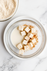 This image shows tofu pieces frying in a skillet of hot oil, turning golden brown and crispy for the vegan fried chicken recipe.