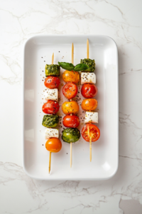 This image shows beautifully garnished Caprese salad skewers with a sprinkle of black pepper and a light drizzle of olive oil, served on a white platter as a delicious appetizer.