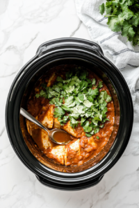 This image shows the finished Crockpot Enchiladas being garnished with freshly chopped cilantro, adding a burst of flavor and a pop of color before serving.