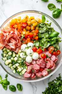 This image shows freshly chopped basil leaves being sprinkled on top of the antipasto salad, adding a burst of herbaceous flavor and a finishing touch.