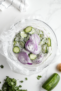 This image shows fresh dill being sprinkled over the cucumber salad, adding a fragrant herb to enhance the flavor of the dish.