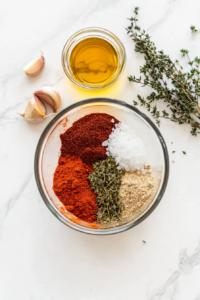 This image shows the ingredients for 15-minute Cajun shrimp, including peeled and deveined shrimp, smoked paprika, garlic powder, onion powder, dried thyme, cayenne pepper, salt, and olive oil, ready to be used.