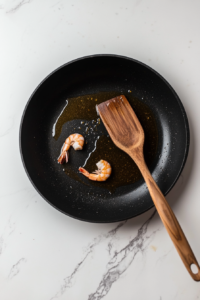 This image shows shrimp being cooked in hot oil in a skillet until they turn pink and are perfectly seared, ready to be added to the fried rice.