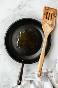 This image shows olive oil heating in a skillet, preparing for sautéing bell pepper, scallions, and shredded cabbage for the keto cabbage rice recipe.