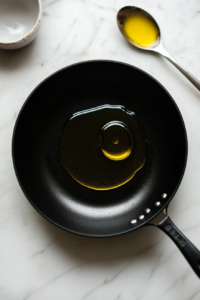 This image shows olive oil heating in a skillet, forming the base for cooking vegetables and shrimp in the Jamaican creamy curry.