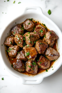 white plate filled with perfectly cooked garlic butter steak bites, garnished with fresh parsley and glistening with a rich, buttery garlic sauce, ready to be served.