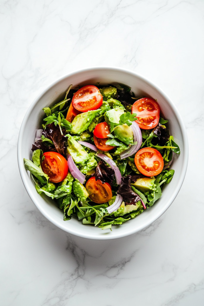 this image shows zesty keto guacamole chopped salad served in a white bowl, topped with slivered red onion and chopped pickled jalapeño peppers.