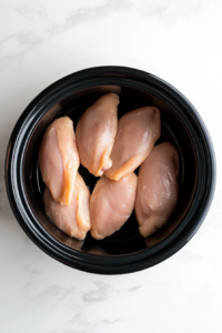 Raw chicken breasts arranged evenly at the base of a Crockpot to start the Italian chicken recipe.