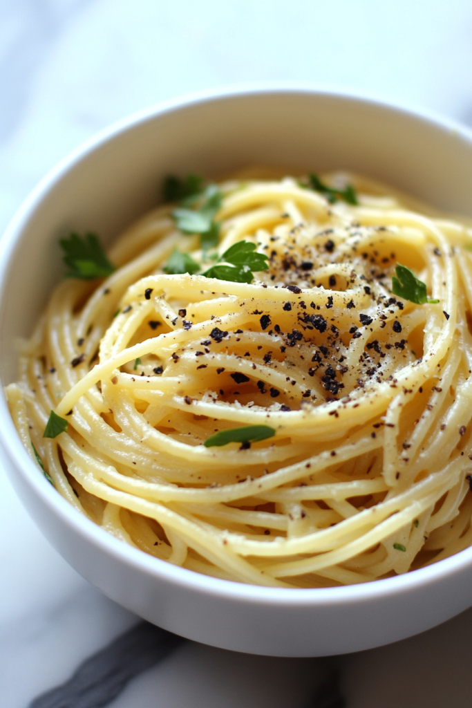 This image shows a serving of lemon pepper pasta in a white round bowl, topped with freshly ground black pepper and a generous sprinkle of Parmesan cheese, creating a light and zesty dish.