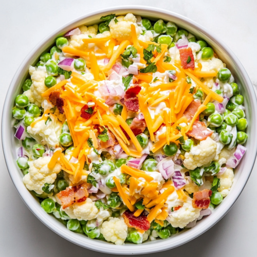 This image shows a white bowl filled with a low-carb pea salad, featuring a creamy dressing that evenly coats the peas, bacon, and cheese, garnished with extra toppings for a delicious presentation, ready to be served as a side dish.