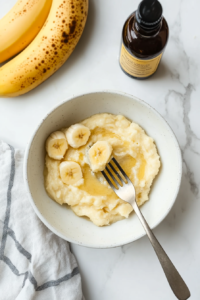 This image shows ripe bananas being mashed in a bowl with vanilla extract added for a rich, aromatic flavor.