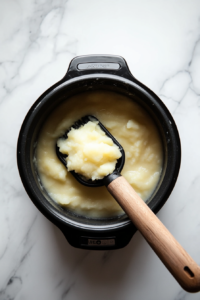 This image shows a potato masher being used to break down the cooked potatoes in the crockpot, creating a creamy base for the soup.