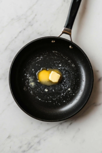 This image shows butter slowly melting in a hot skillet, preparing a rich base for cooking shrimp for the enchilada filling.