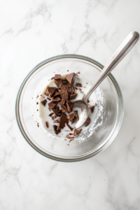 This image shows pieces of dark chocolate being melted into warm coconut milk, creating a velvety and rich filling for the vegan chocolate tart.