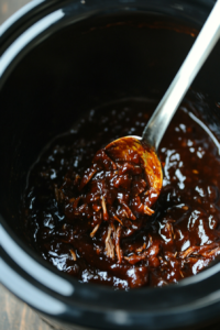 This image shows the shredded pork being mixed thoroughly with BBQ sauce in a bowl, coating every piece evenly with the tangy glaze.