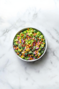 This image shows the prepared creamy dressing being poured over the broccoli salad, followed by tossing the ingredients together until everything is evenly coated.