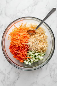 This image shows shredded cabbage, julienned carrots, and broken ramen noodles being combined in a large bowl to create the base for the simple oriental Asian cabbage salad.