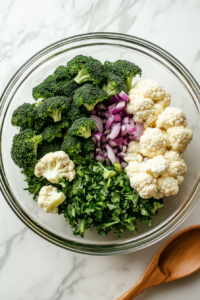 this image shows a large bowl filled with broccoli, cauliflower, and red onion, mixed together for the base of the salad.