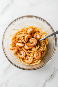 This image shows cooked pasta being combined with sautéed shrimp in a large skillet, ready to be coated with the creamy Bang Bang sauce.